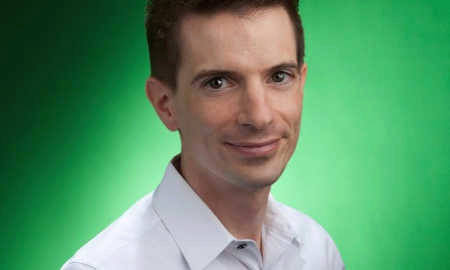 A headshot of a person with short dark hair, wearing a light-colored shirt, against a bright green background.