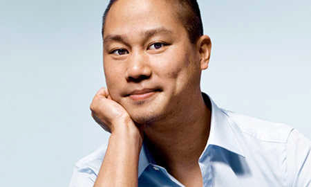 Headshot of a person with a slight smile, resting their chin on their hand, wearing a light blue collared shirt, against a pale background.