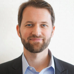 Matthew Killingsworth A headshot of a person with short brown hair and a beard, wearing a dark blazer and a light blue collared shirt, against a plain background.