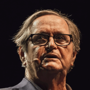 brianlittleheadshot An older person wearing glasses and a microphone headset, possibly speaking or presenting in a professional setting.