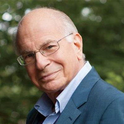 Headshot of an older person wearing glasses and a suit jacket, standing outdoors with blurred greenery in the background.