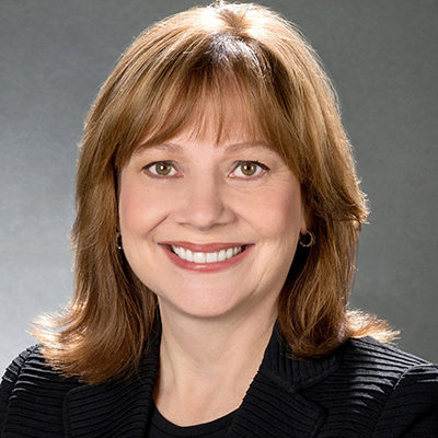 Headshot of a person with medium-length brown hair, smiling, wearing a black blazer and a dark top, set against a neutral background.