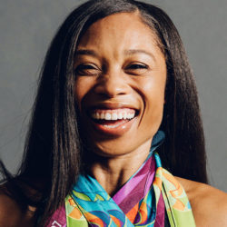 A person smiling broadly, wearing long dark hair and a vibrant, colorful scarf.