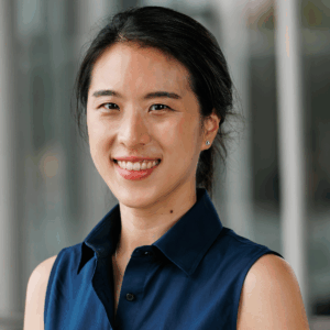 Kwon 4x5 Headshot of a smiling person with dark hair in a ponytail, wearing a sleeveless navy shirt, against a blurred background.
