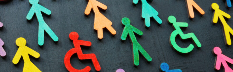 Colorful wooden figures of people, including symbols representing individuals with disabilities, on a dark background, symbolizing diversity and inclusion.